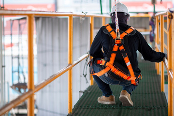 Construction worker in harness and safety line holding onto rail Construction worker in harness and safety line holding onto rail