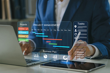 Person in blue suit in front of laptop with stylus in hand writing on tablet and project management screen superimposed Person in blue suit in front of laptop with stylus in hand writing on tablet and project management screen superimposed