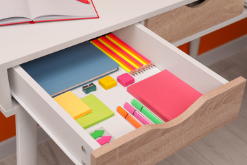open drawer in a desk with colorful sticky notes, paper, and pencils